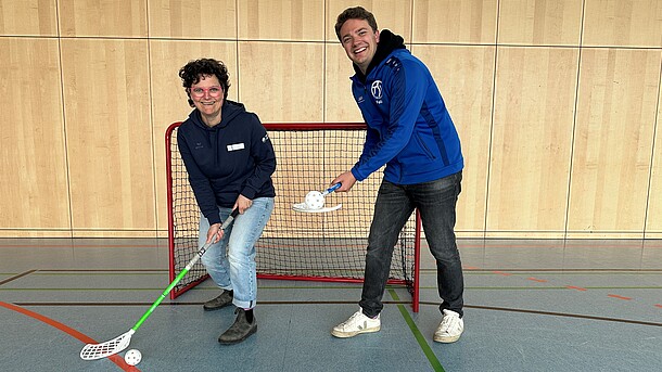 Eine Spielerin und ein Spieler präsentieren Floorball in der Halle.