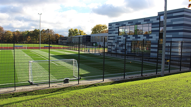 Der SportCAMPUS des ZfH vom Kunstrasenplatz aus gesehen. Man sieht ein Gebäude und die Tartanbahn.