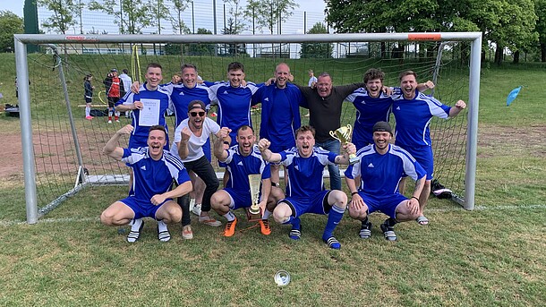 Fußballer stehen jubelnd im Tor und halten den Pokal in die Höhe