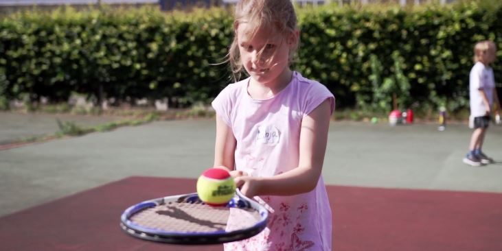 Ein Kind balanciert einen Ball auf einem Tennisschläger.