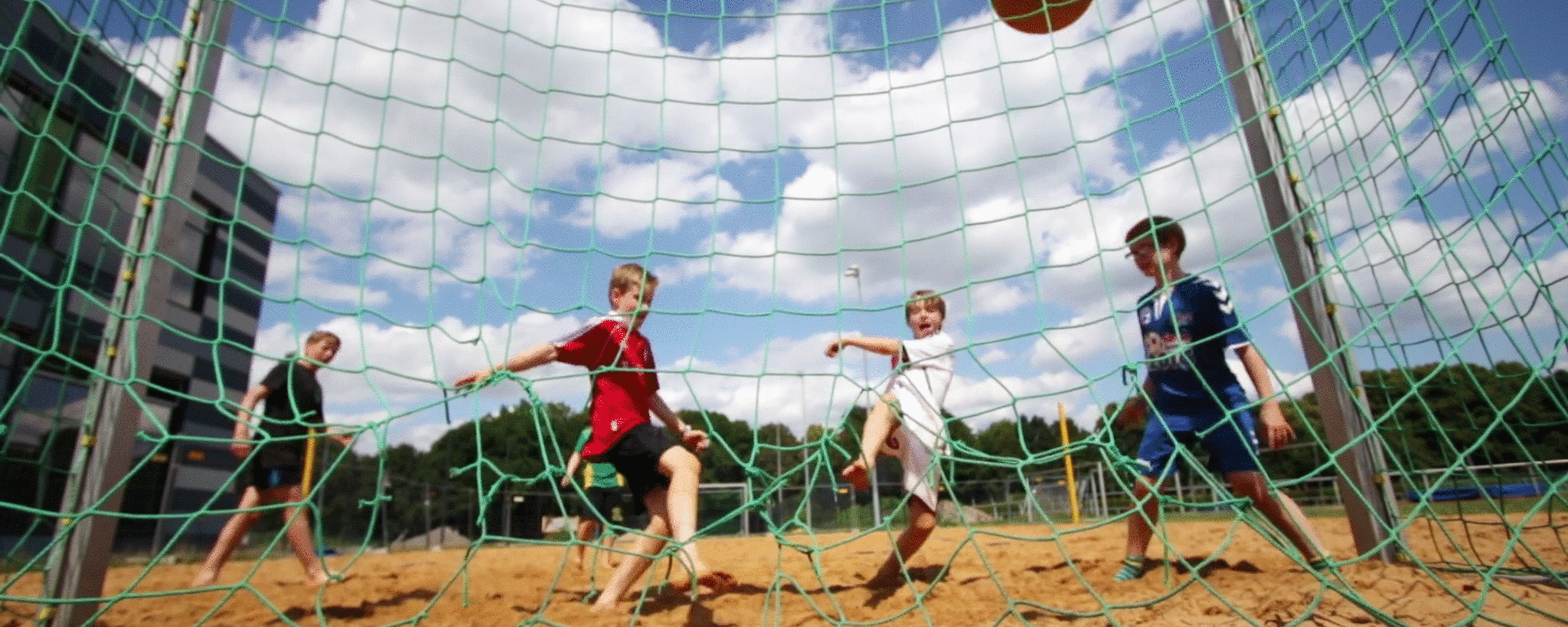 Eine Gruppe Kinder schießt einen Ball in ein Tor.