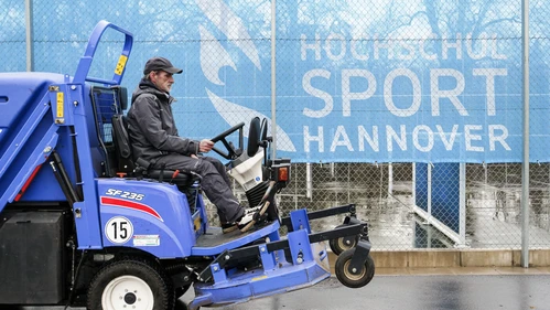 ein technischer Mitarbeiter sitzt auf einer Säuberungsmaschine und fährt über den SportCAMPUS
