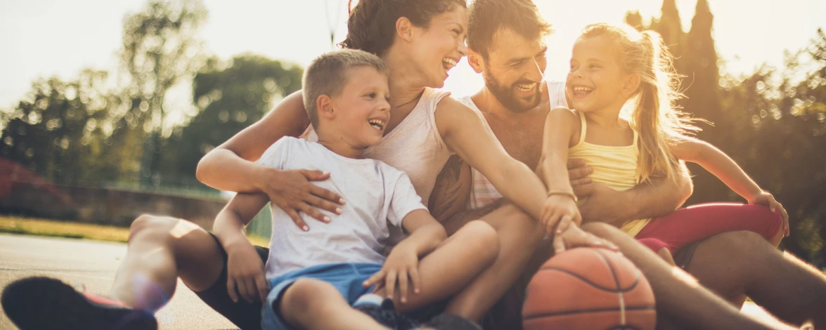 Familie mit zwei Kindern sitzt gemeinsam auf einem Basketball Court.