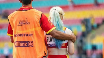 Ein Assistent legt den Arm um eine Sportlerin mit Handicap während eines Turniers.