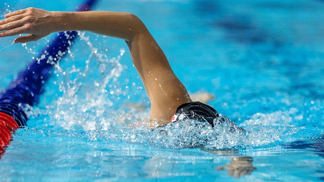 schwimmende Person, die mit Kraulschlag des rechten Arms auf uns zuschwimmt. Kopf ist unter Wasser.