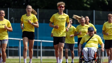 Das Bild zeigt eine inklusive Gruppe beim gemeinsamen Sport auf der Laufbahn auf dem SportCAMPUS. Alle tragen gelbe „let’s IDUS“-Shirts; Teilnehmende laufen und eine Person ist im Rollstuhl dabei. Die Stimmung wirkt motiviert und gemeinschaftlich.
