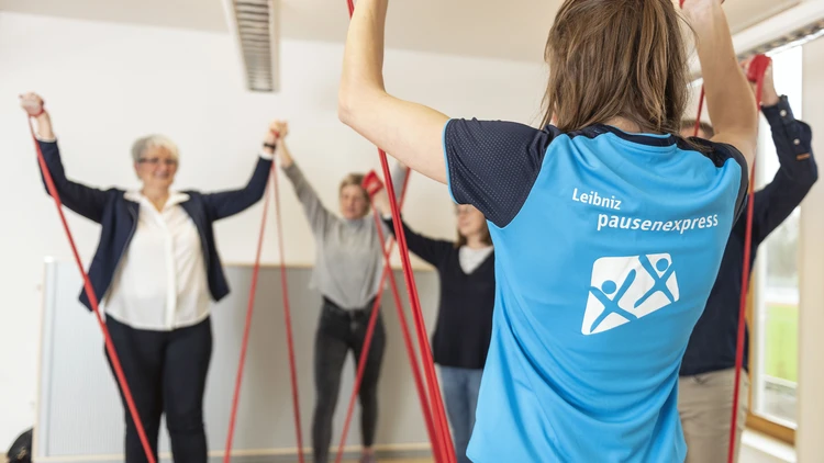 Eine Übungsleitende macht eine Fitnessübung vor, die die Teilnehmenden ausführen.