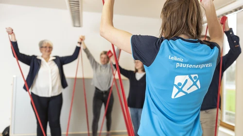 Eine Übungsleitende macht eine Fitnessübung vor, die die Teilnehmenden ausführen.